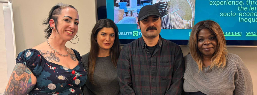 A group shot showing the four members of the Community Reporter team in Birmingham. They are standing in front of a data screen and smiling at the camera.